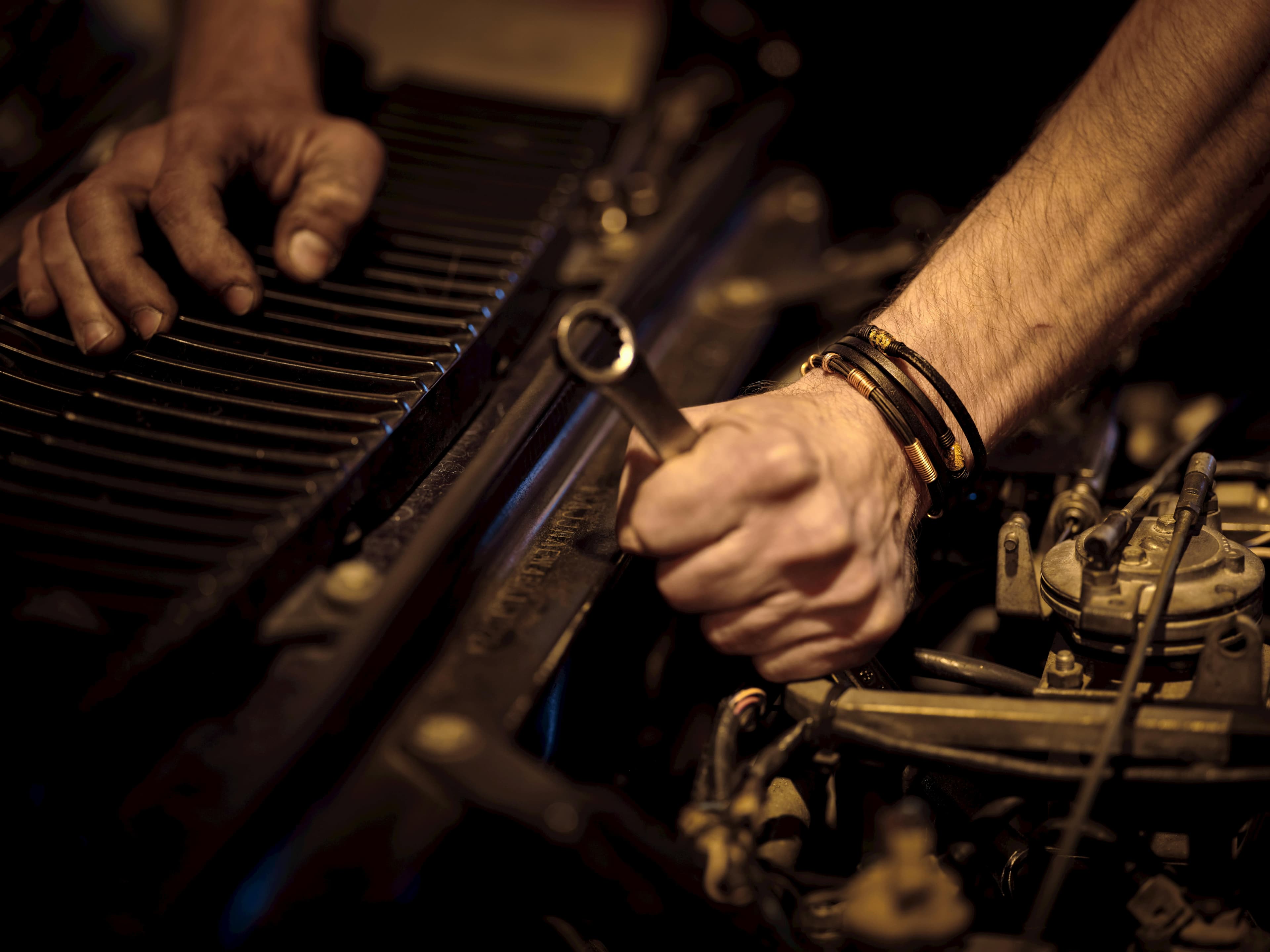 Mechanic's hands tightening a bolt under a hood with a wrench